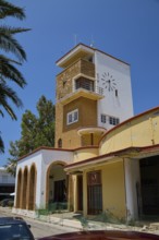 Market hall, agora, clock tower in yellow and red with palm trees and arches, embedded in a green