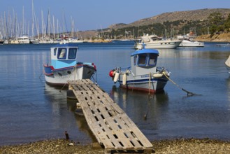 Two colourful boats on a wooden jetty with blue water and yachts in the background, Lakki, Leros,