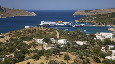 Large ferry in front of a coastal settlement on a hill with blue sea in the background, Lakki,