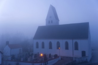 St. Martin's parish church with cemetery, orange-coloured street lamps in the morning fog in front