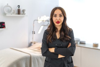 Confident female beautician standing with crossed arms in her modern beauty salon, representing