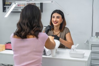 Smiling manicurist applying nail polish to her customer in a beauty salon, performing a