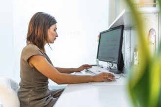 Beautician using a desktop computer, managing appointments and customer data in a bright and modern