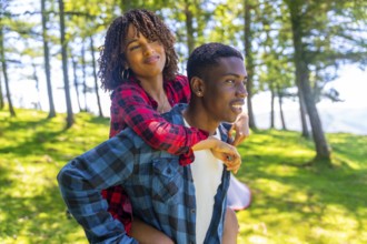Young man giving piggyback ride to his girlfriend in forest during camping trip, enjoying summer