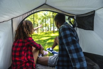 Two tourists sitting inside their tent, excitedly pointing at something intriguing in the lush