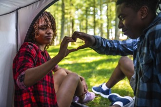 Young campers making heart shape with hands while sitting in tent during camping trip in forest