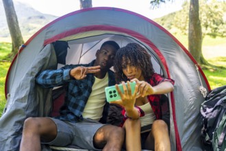 Two young campers are taking a selfie inside their tent, enjoying a fun camping trip in nature