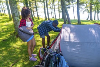 Couple setting up a tent in a lush forest, preparing their campsite for a summer adventure filled