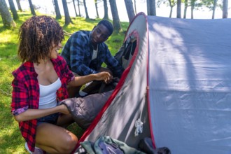 Young black couple enjoying the outdoors while setting up a camping tent in the forest, placing a
