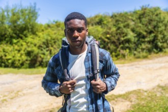 Confident young hiker wearing a backpack, enjoying a sunny day while discovering a beautiful nature