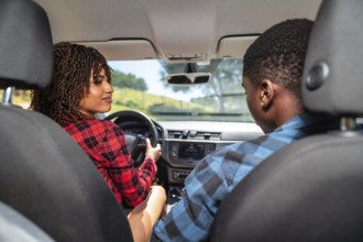 Young black couple driving a modern car on a sunny day, laughing and enjoying every moment of their
