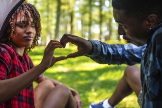 Happy couple making heart shape with hands while camping in nature, enjoying a romantic moment