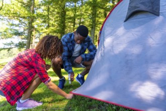 Young campers pitching tent on campsite during summer vacation in forest enjoying outdoor lifestyle