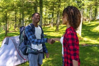 Two hikers shaking hands near tent in forest, enjoying camping trip and celebrating teamwork and