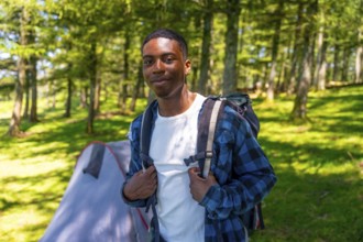 Young black man wearing a backpack, enjoying a camping trip in the woods, surrounded by lush trees