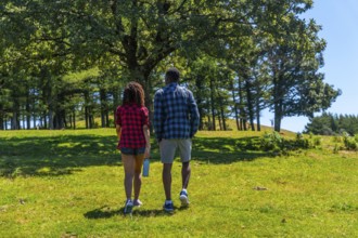 Couple walking on green meadow in mountain on sunny summer day, enjoying the nature, seen from