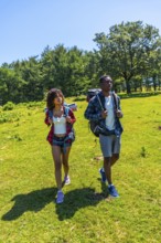 Young hikers walking in a green meadow by a forest on a sunny day, enjoying the beautiful nature