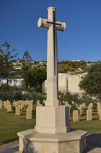 A high stone cross in a well-kept peaceful military cemetery under a clear blue sky, Military