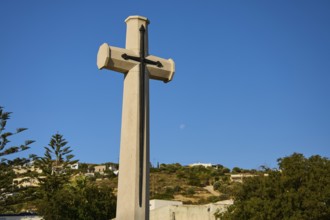 Large cross in front of blue sky with moon, landscape in the background, military cemetery,