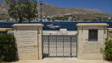 Stone gate of a cemetery with sea view and memorial inscription, mountains in the background,