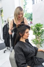 Hairdresser styling client's hair with curling iron in modern beauty salon, creating fashionable