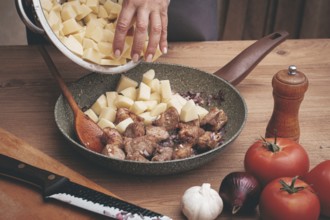 Potato slices are laid out in a frying pan, with browned meat, cooking stewed meat with potatoes