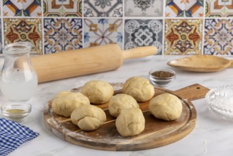 Several dough balls on a round wooden board, surrounded by baking utensils