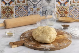 Dough on a wooden board with rolling pin and bowls in front of colourful tiles
