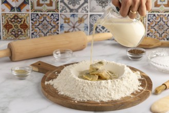 Milk is poured into a well of flour on a wooden board, surrounded by ingredients