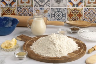 Pile of flour on a wooden board surrounded by various baking ingredients in a kitchen