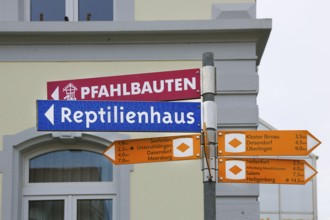 Sign, signpost, pile dwellings, reptile house, arrow, several signposts with distance, writing,