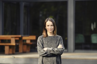 A young woman with shoulder-length hair stands confidently with her arms crossed outside a sleek,
