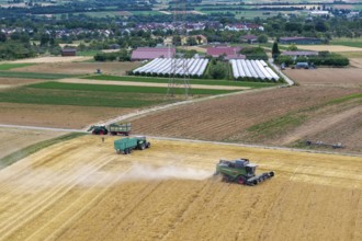 A combine harvester and tractor operate in a field in a rural area near a village