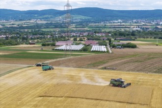Wide fields with combine harvesters and tractors against a backdrop of mountains and a power pole,