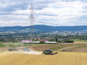 A combine harvester works near a power pole in a vast rural landscape under cloudy skies, Traktore