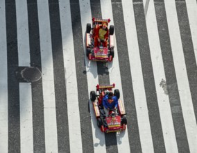 People in costumes drive small go-kart racing cars across zebra crossings, Shibuya Crossing,