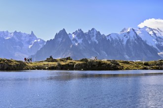 A group of hikers at Lac de Chésserys, behind the snow-covered Mont Blanc massif,