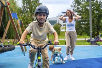 Happy children enjoying riding bicycles in a modern playground while their mother watches over