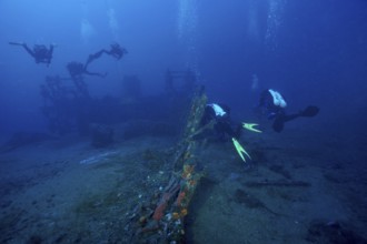 Divers explore a wreck covered with sea sponges on the ocean floor in deep blue water in the
