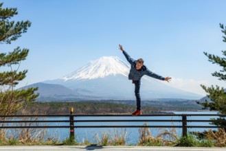 Young man balancing on railings next to a road, view across the lake to Mt Fuji volcano, Motosu