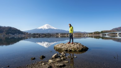 Young man standing on a rock in water, volcano Mt. Fuji is reflected in Lake Kawaguchi, Yamanashi