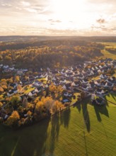 Idyllic village in autumn light with many houses and surrounding fields, surrounded by forests,