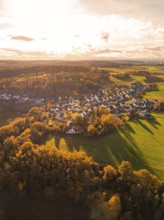 Autumn landscape with a village flooded with warm light, surrounded by fields and forests,