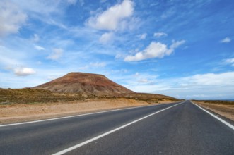 View of long straight paved road to the left partly eroded volcano volcanic cone in volcanic