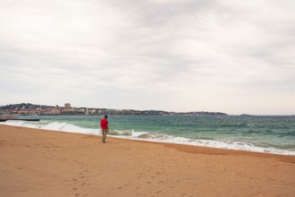 Man wearing a red shirt looking at the moving sea, Fréjus in the background, Provence-Alpes-Côte
