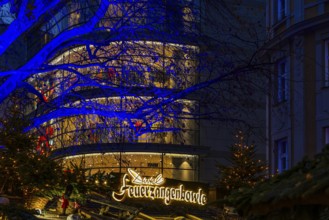 Sales stand for Feuerzangenbowle, above a deciduous tree illuminated with blue light,