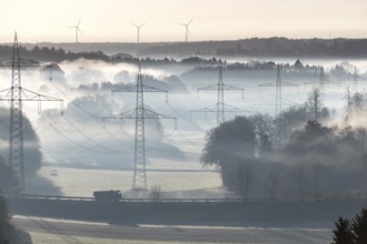 Misty morning landscape with power poles in the foreground and wind turbines, Swabian Jura,