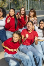 Group of diverse young women friends wearing red shirts and face paint, sitting together and