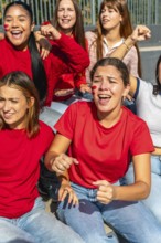 Group of enthusiastic young women friends wearing red shirts and face paint, actively cheering and