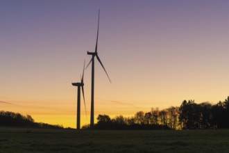 Two wind turbines in front of a devotional sunset. The distinctive silhouettes stand out clearly,